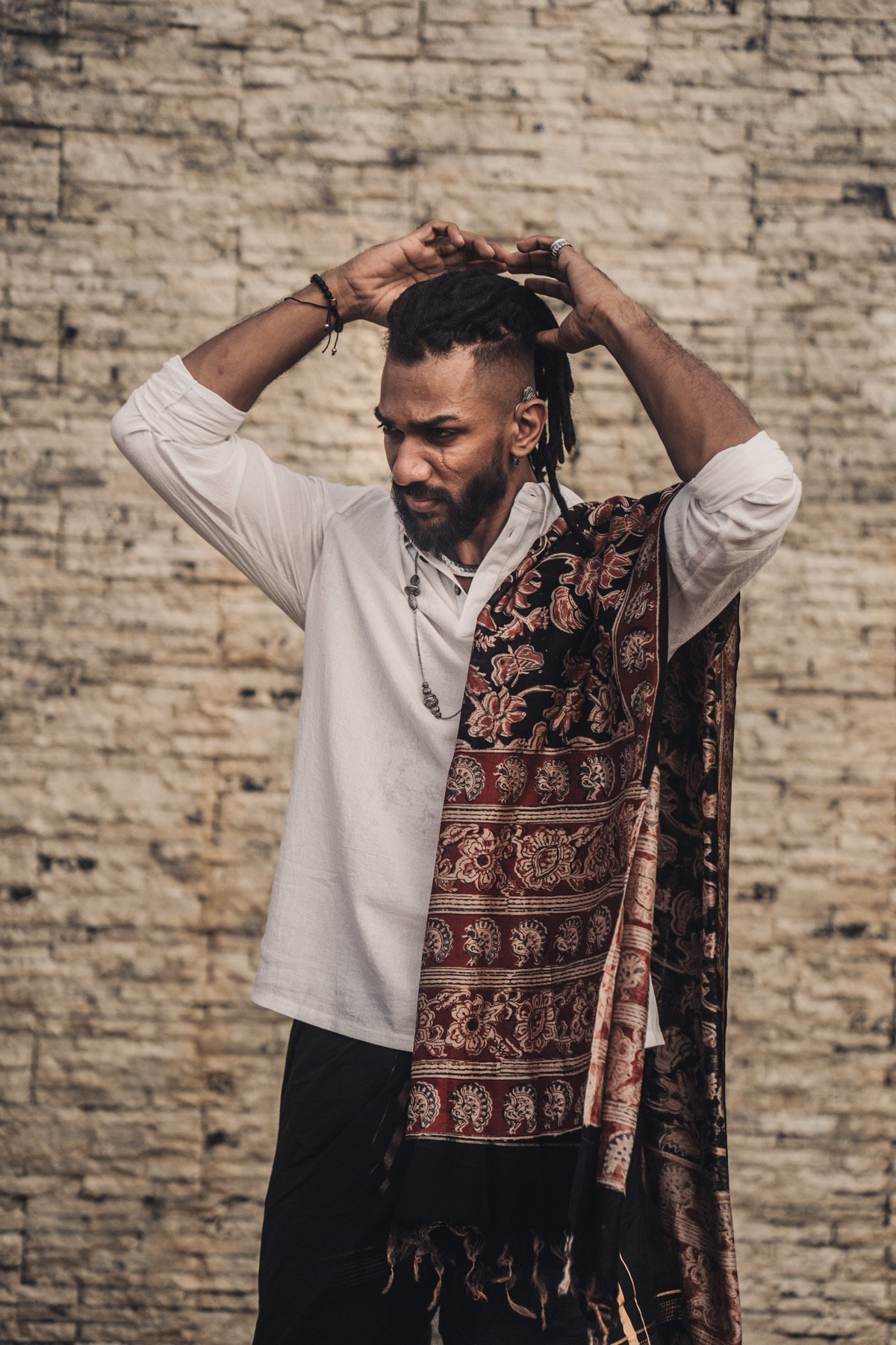 Theebaan G in a white shirt and patterned shawl against a brick wall
