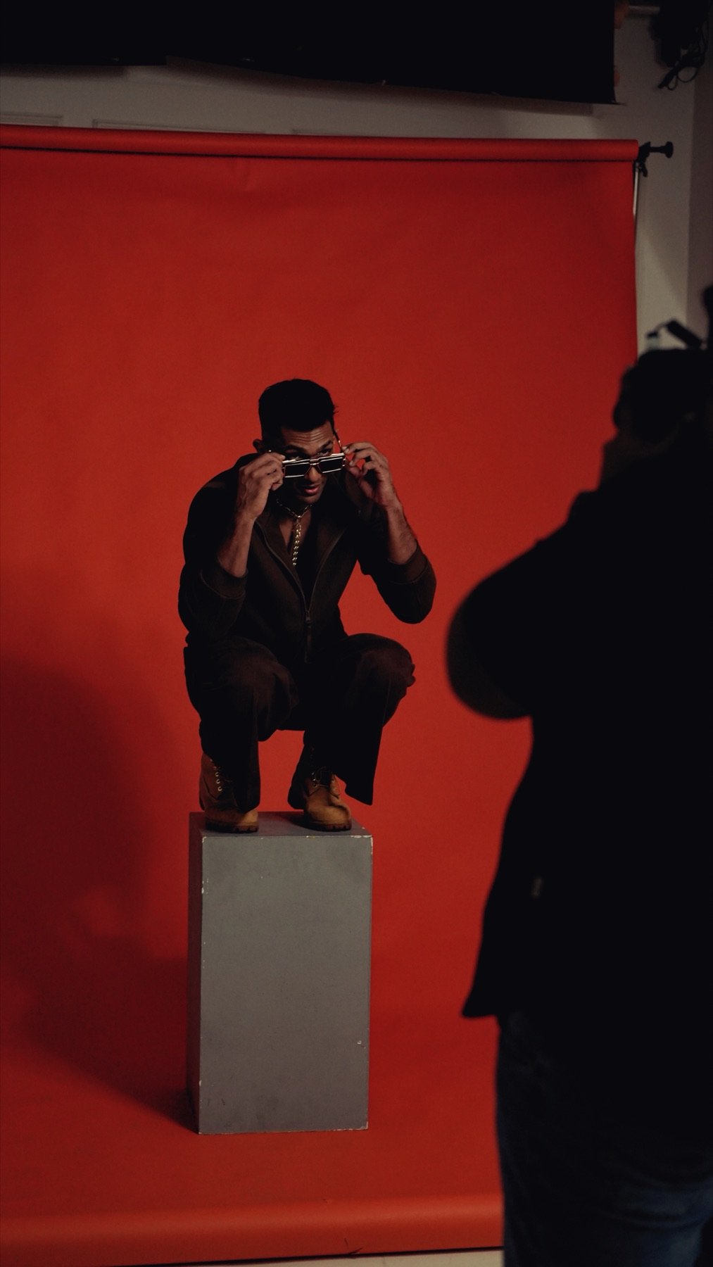 Theebaan G crouched on a plinth against a red studio backdrop