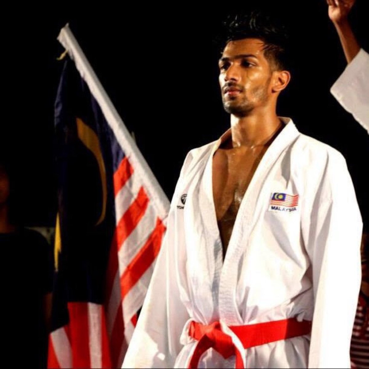 Theebaan G in a karate gi beside the Malaysian flag before a bout